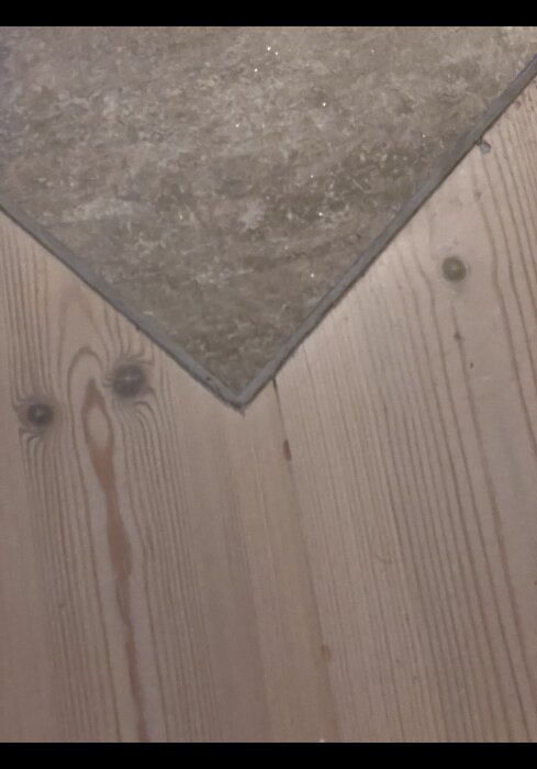 Närbild av hörna med mörk stenplatta och ljust trägolv.