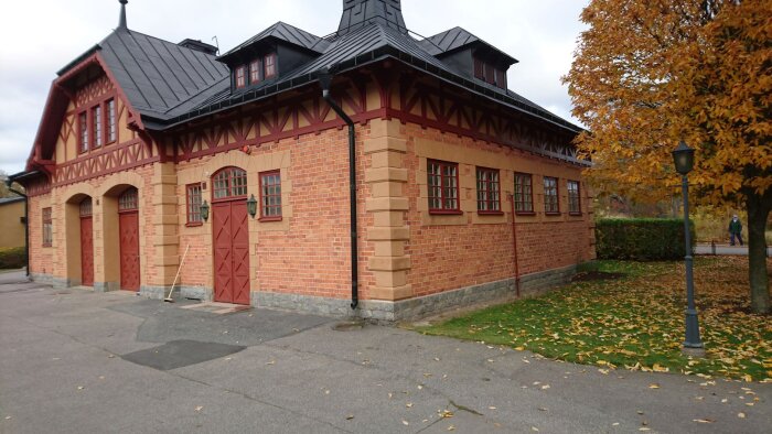 Gammalt tegelstall med trädetaljer vid Täcka udden, omgiven av höstlöv och lampa.