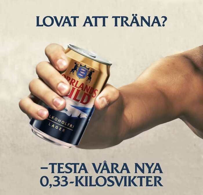 En hand håller en ölburk med texten "Norrlands Guld Alkoholfri Lager", omgiven av texten "Lovat att träna? Testa våra nya 0,33-kilosvikter".