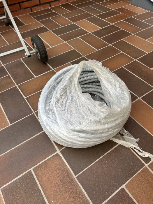 Rulle med NKT Prefix 20mm slang på en terrakottafärgad plattlagd yta, delvis inplastad.