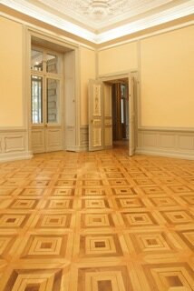 Rum med exklusivt parkettgolv i avancerat mönster, typiskt för eleganta byggnader som palats och ambassader; ljusa väggar, trätak och fönsterdörr.