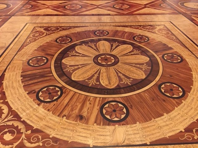 Detaljerat mönstrat trägolv med intrikata blom- och geometriska motiv, typiskt för palats eller ambassader.