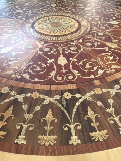 Intrikat designat massivt trägolv med cirkulärt blommönster och inläggningar, likt dem i exklusiva byggnader som palats och ambassader.