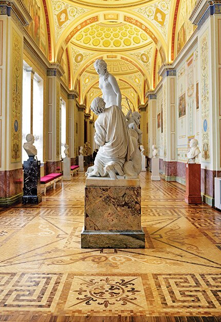 Invecklat mönstrat trägolv i magnifik hall med klassiska statyer och dekorerade valvtak.