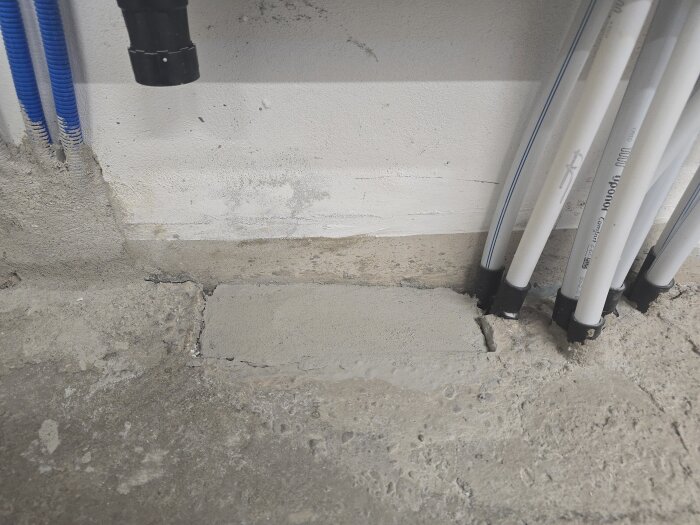 Vitt och grått rörsystem installationsområde på vägg med nylagt murbruk synligt vid golvet.