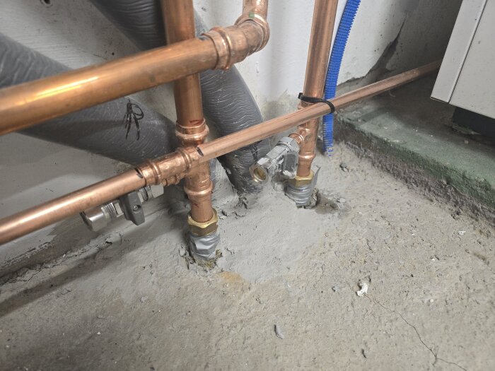 Kopparrör i ett källarutrymme med cement runt basen; området är delvis grundmålat.