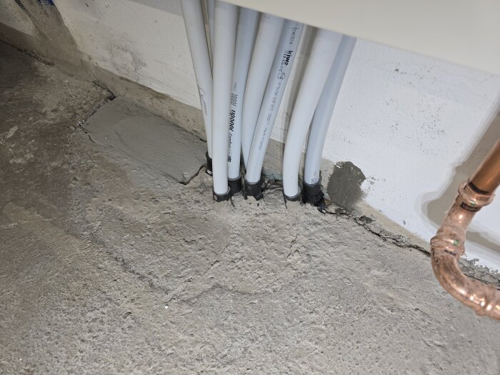 Nyblandat lagningsbruk applicerat kring rör i en källare. Bruket har torkat och täcker nu hålrummet bakom radiatorrören och väggen är grundmålad.