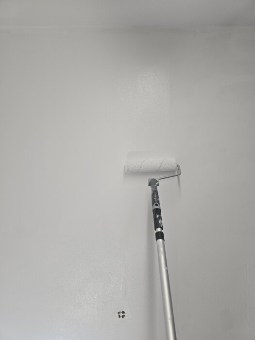 Målning av vägg med roller där ett lager vit grundfärg appliceras.