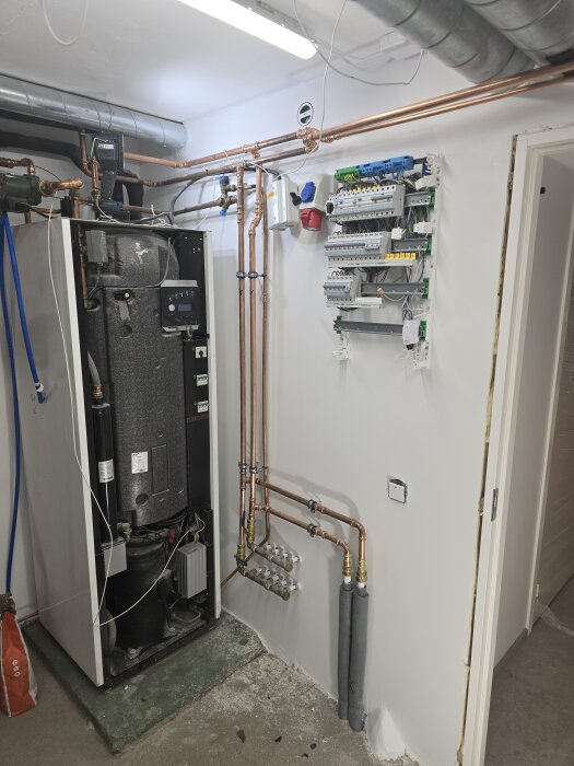 Värmepump och kopparrör installerade i ett rum med nymålade vita väggar och blottlagd elcentral.