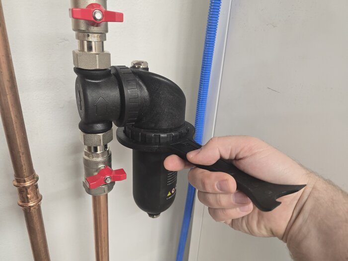 Hand skrapar bort magnetit från ett filter i värmesystem med plastskrapa.