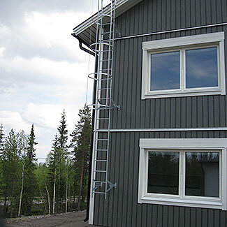 Fasadstege monterad på husets gavel, omgiven av träd och klara himmel.