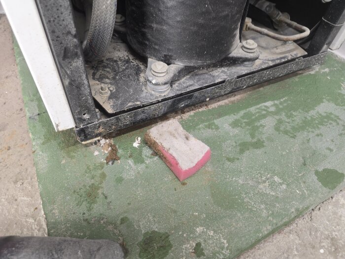 Grön sockel under en värmepump med smuts och en rödvit svamp intill; del av renoveringsprojekt.