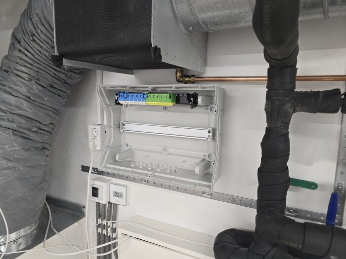 Säkerhetsbrytare och öppen elcentral med ledningar, rör och ventiler i ett rum under renovering.