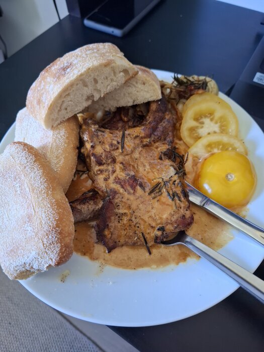 En tallrik med fläskkarré i gräddsås, två halvor ciabatta och skivade tomater.