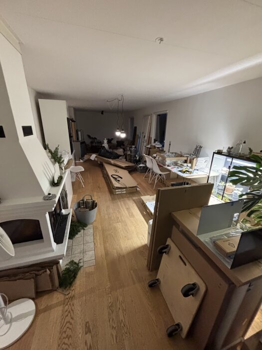 Rum under renovering med verktyg och byggmaterial på golvet, flera stolar och en arbetshörna syns i bakgrunden.