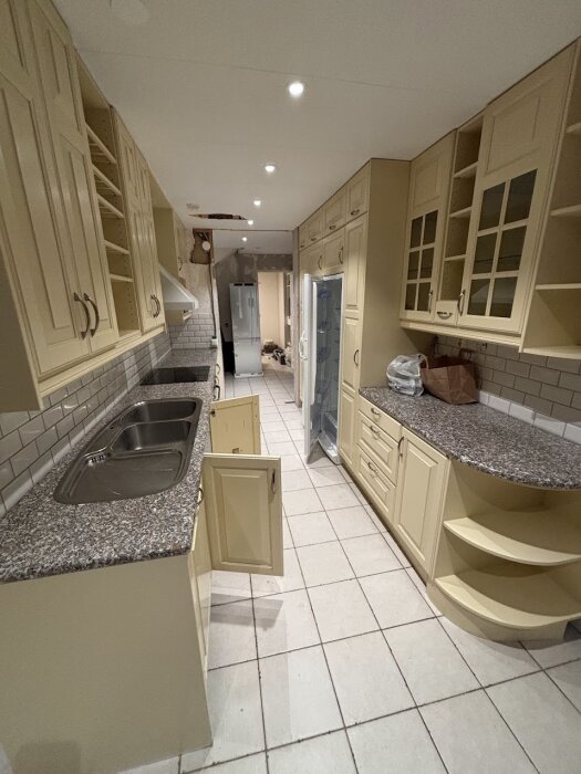 Gammalt kök med ljusa skåpluckor, granitbänkskivor och kaklade väggar, redo för renovering och modernisering.