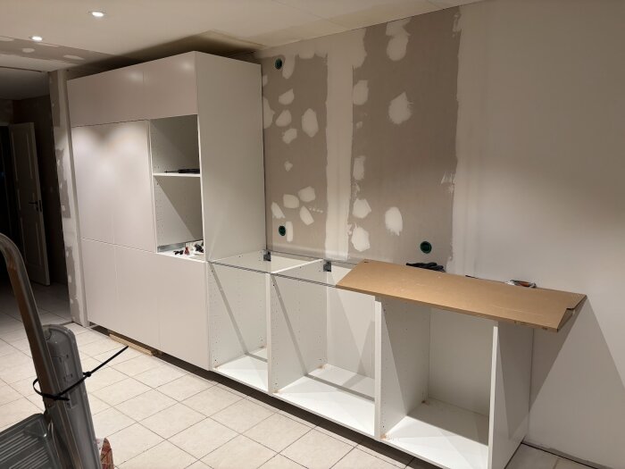 Köksrenovering pågår med uppsatta gipsskivor och vita stommar. En MDF-skiva ligger ovanpå, rum i modern stil under konstruktion.