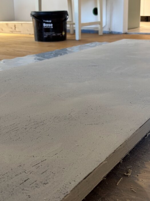 Bänkskiva av laminatskiva behandlad med microcement ligger på golvet, med en burk bas cachment i bakgrunden.