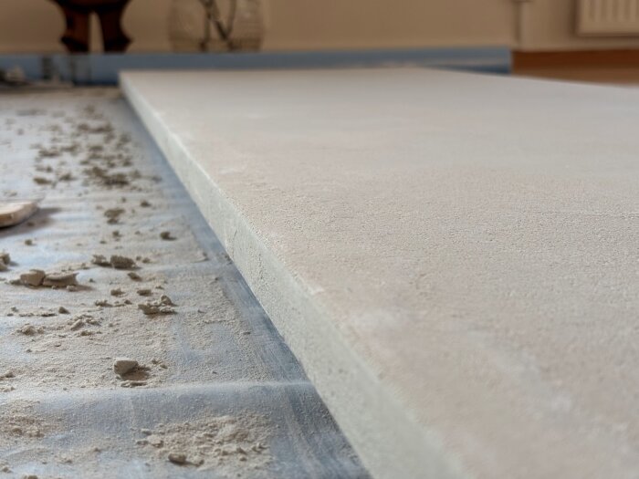 Närbild av en bänkskiva täckt med microcement, omgiven av byggdamm, under renoveringen av ett kök.