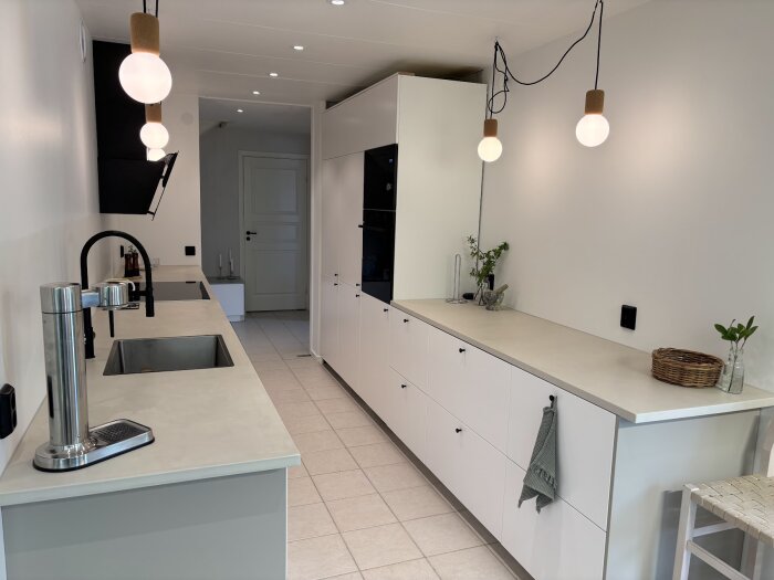 Modernt kök med ljusa laminatbänkskivor behandlade med mikrocement, enkel belysning, diskho, kran och minimalistiska vita skåp.