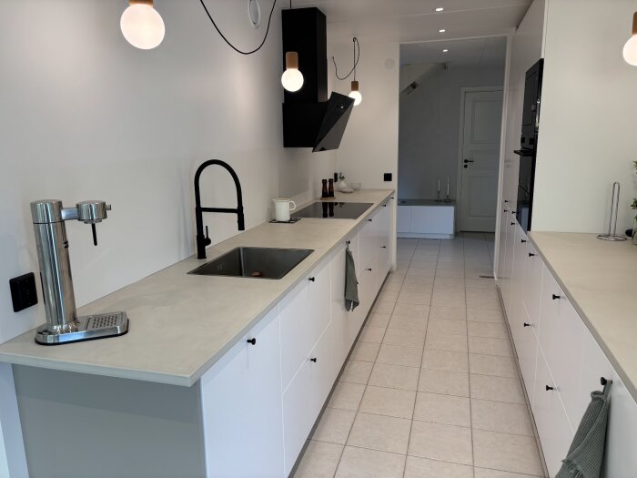 Modernt kök med minimalistisk inredning, vita skåp, microcement-bänkskivor, svart blandare, och enkla lampor.