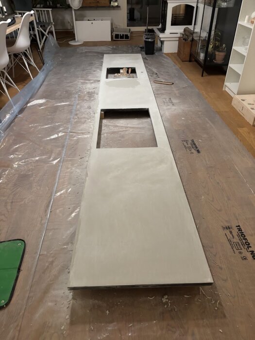 En lång bänkskiva av laminat behandlad med microcement ligger på golvet, med hål för spishäll och diskho, redo att installeras i ett modernt kök.