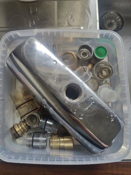 Metallföremål och rördelar i en plastlåda fylld med vätska för rengöring, förberett för ättiksbad i ett renoveringsprojekt.