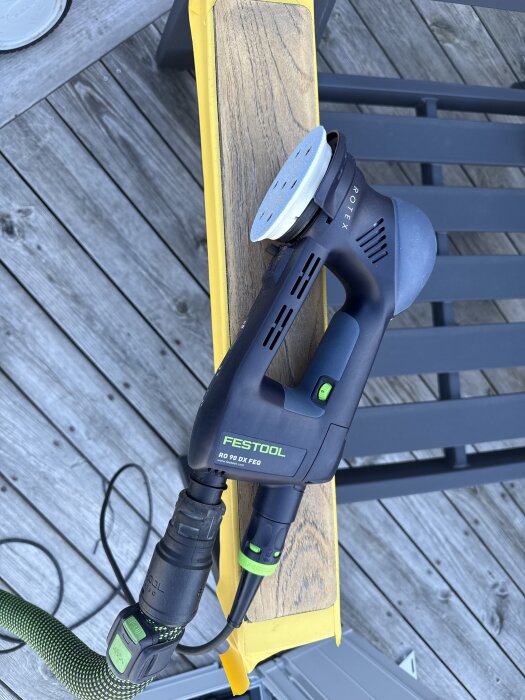 Festool slipmaskin RO 90 DX FeQ på ett trästycke med gul tejp på en trätrall.