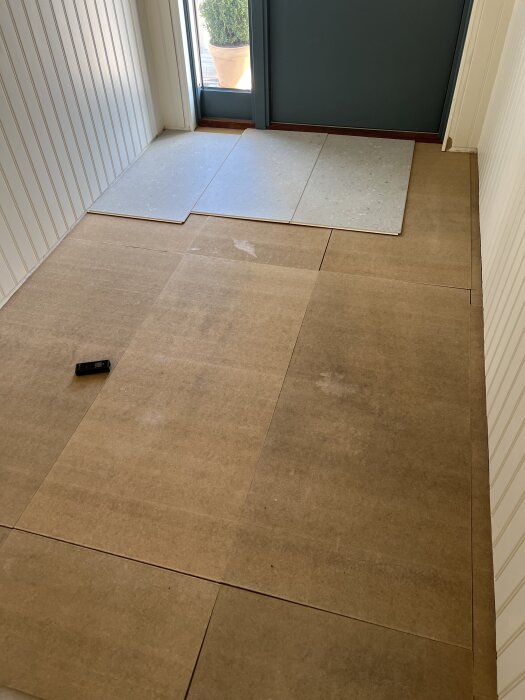 Golvläggning med skivor på golvet i hallen, med ett måttband och dörr i bakgrunden.