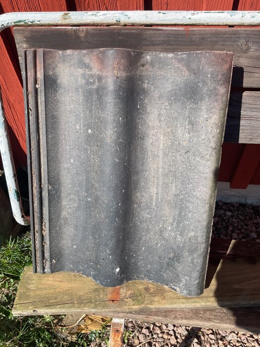 En oanvänd, svart betongpanna märkt diamant lutad mot en röd trävägg utomhus.