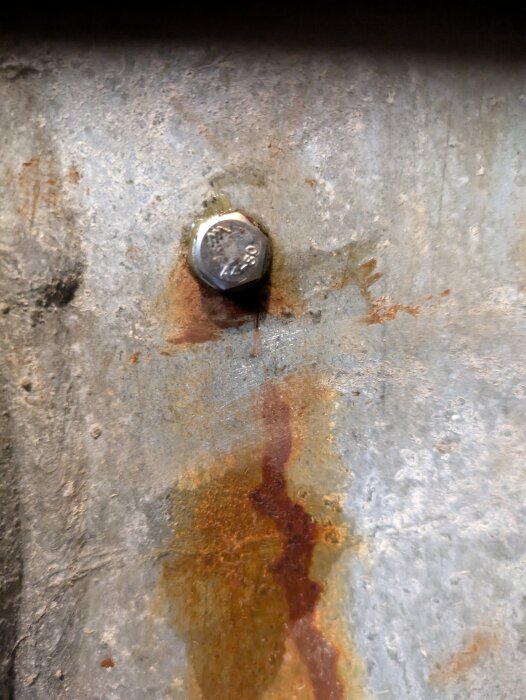 Närbild av en bult med synlig rostfläck på en metallisk yta, nära en inspektionslucka.