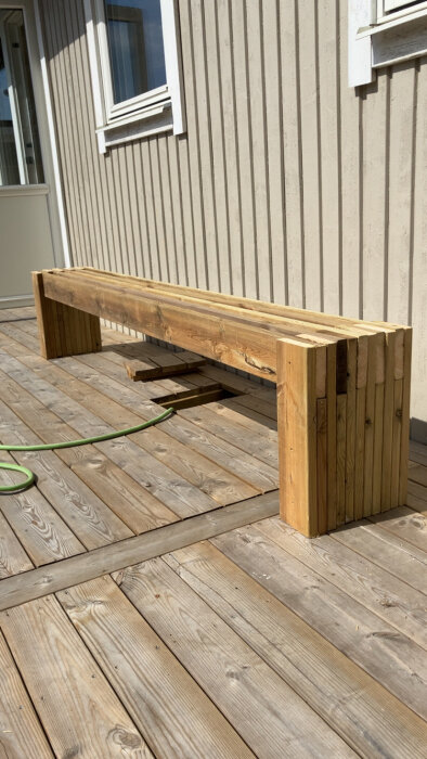 Bänk tillverkad av överbliven trall, placerad på en altan; kan behöva en extra längd och slipning.