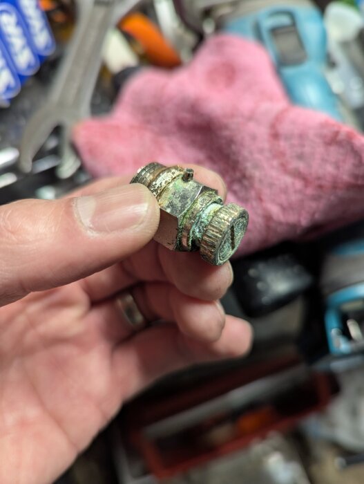 Korroderad automatisk avluftare hålls i handen mot bakgrund av verktyg och trasor.