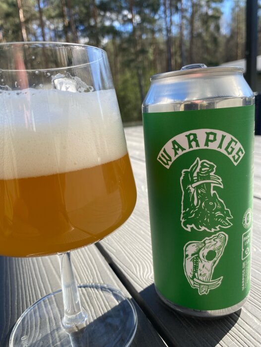 Ett glas öl och en burk med etiketten "Warpigs" står på ett bord utomhus i solen.
