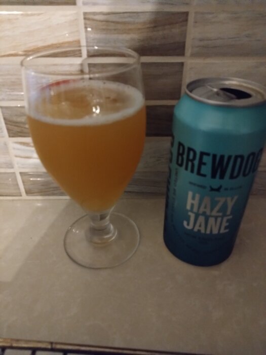 Glas och burk med BrewDog Hazy Jane öl på en köksbänk med kaklad vägg bakom.