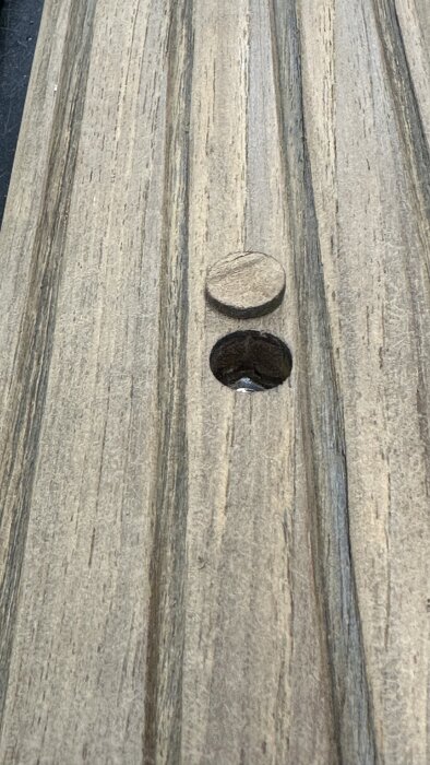 Steg av teak med borrat hål och lös plugg, visar tidigare infästning av stege, inför byte och montering av nya teakpluggar med epoxy.