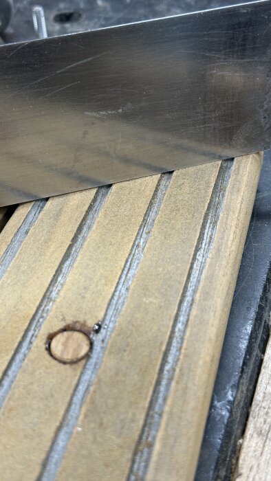 Närbild av träplanka med frästa spår, ett borrat hål och verktyg i metall ovanpå, del av renoveringsarbete.
