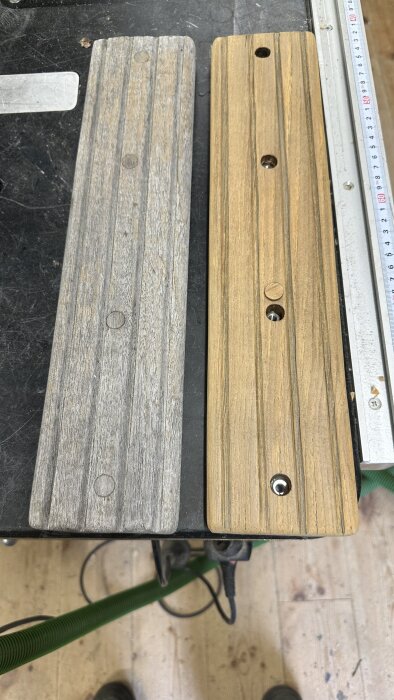 Två trappsteg i trä, ett grått och slitet, det andra nyrenoverat och behandlat, liggandes på ett arbetsbord. En linjal syns bredvid.