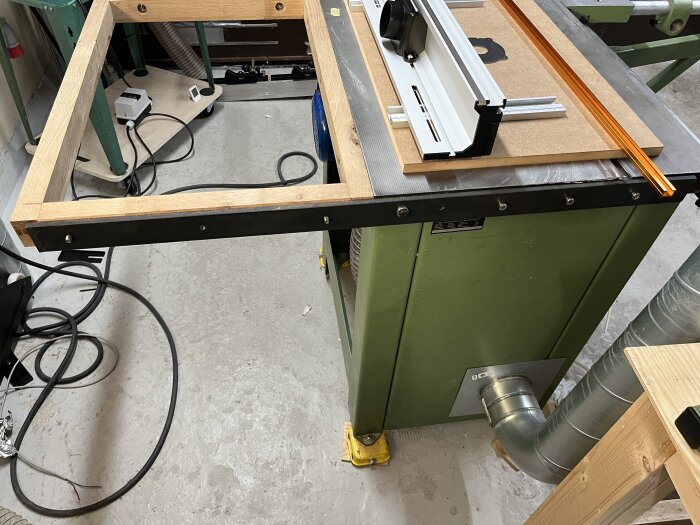 Verkstad med grönt fräsbord, trästomme och tillbehör för bordsbreddning samt dammsugaranslutning, set up för framtida verkstadsprojekt.