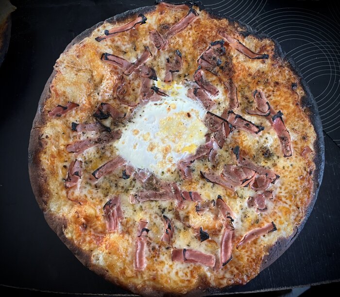 Hemlagad pizza med bränd kant, toppad med ost, skinka och ett krämigt ägg i mitten, på en bakplåt utan förpackning.