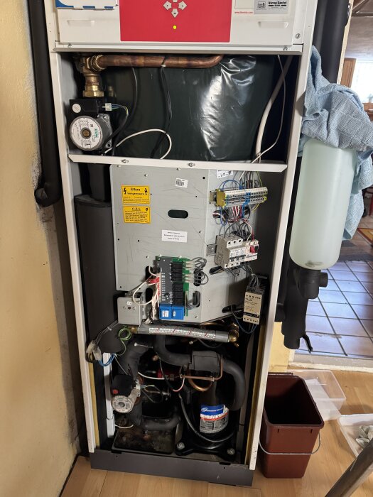 Inre delen av en Thermia Diplomat värmepump visas, med synliga rör, sladdar och komponenter för felsökning och underhåll.