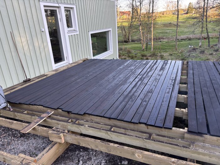 Trädeck under uppbyggnad vid husfasad, brädor behandlade med linolja och terpentin, förberett för terrass.
