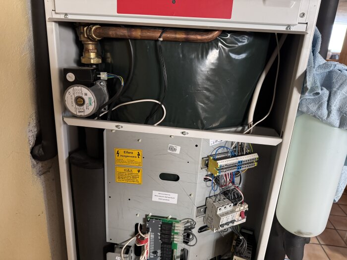 En öppen panel på en Thermia Diplomat värmepump visar rör, kablar och elektriska komponenter.