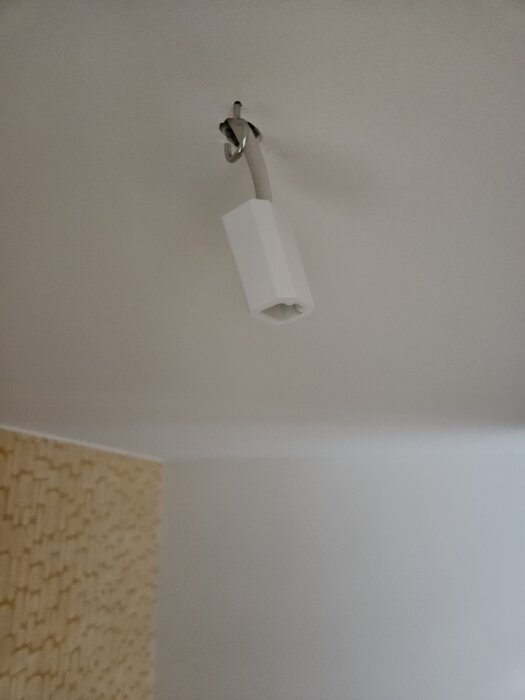 Taklampa med hängande kabel och krok som ser instabil ut.