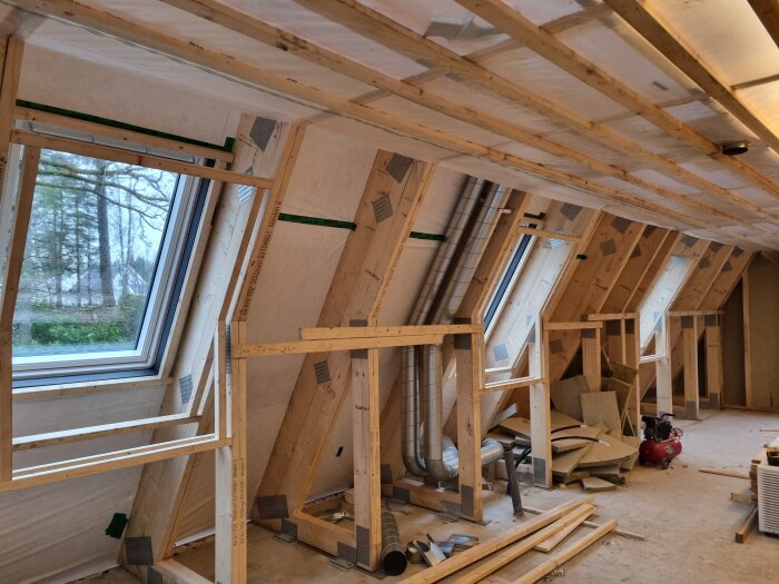 Träramar byggda runt takfönster i ett halvfärdigt rum, isoleringsmaterial och verktyg synliga på golvet.