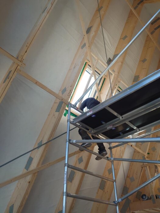 Person arbetar på en byggställning nära ett takfönster i ett isolerat trätak under konstruktion.