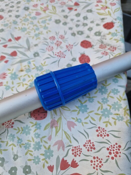 Blå plastlåsring på aluminiumskaft ligger på ett blommigt bord.