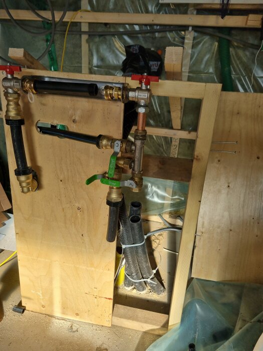 Vattenmätarvägg med rörkopplingar i garage, byggd av plywood och ansluten med olika rör och ventiler, del av ett renoveringsprojekt.