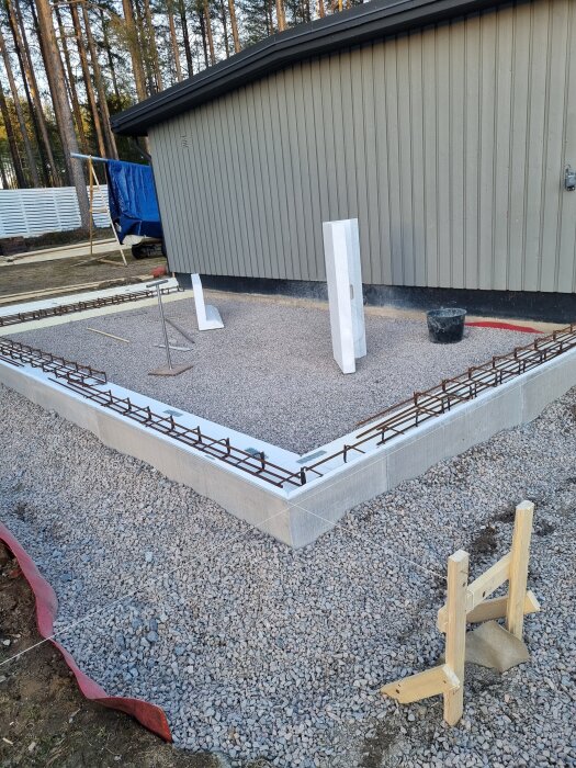 Grundarbete med grus och form för betonggjutning vid byggnad. Armeringsjärn på plats och väderfrågor diskuteras.