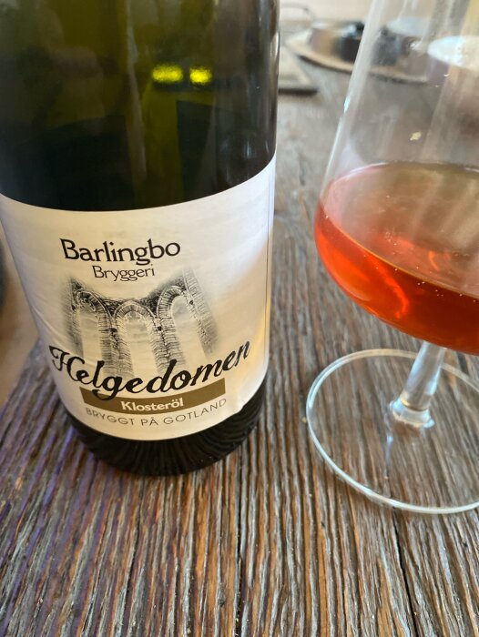 Flaska med Barlingbo Bryggeri Helgedomen Klosteröl och glas med klosteröl på rustik träyta.